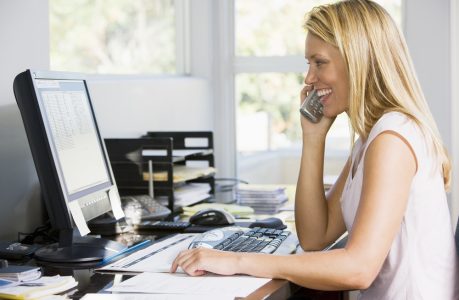 Woman in home office with computer using telephone smiling